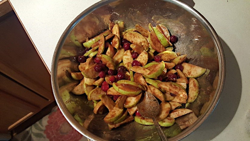 Apples. cranberries, flour, and spices mixed in a bowl